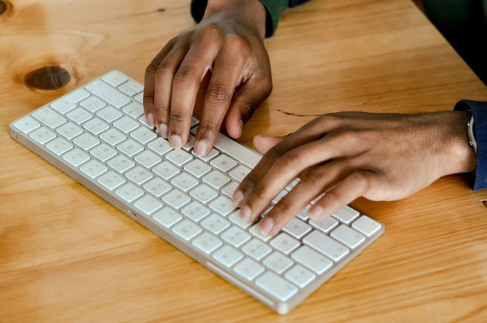 木の机の上の白いキーボードを、両手で打っている手元